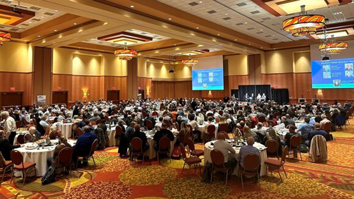 People sitting at tables in a conference room listening to a speaker on the stage