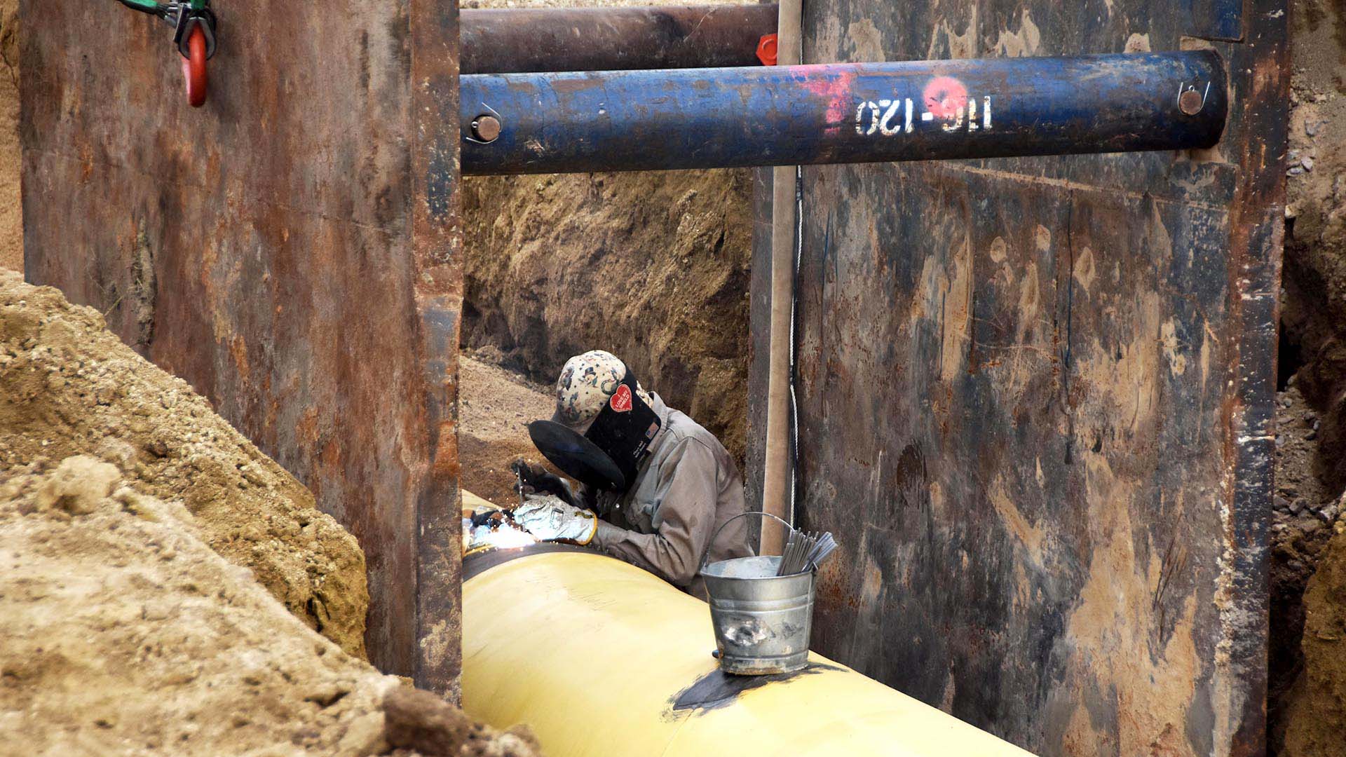A man welding on a water pipe in ground.