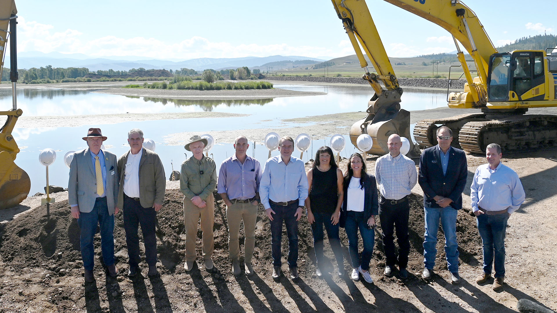 People lined up in front of a reservoir. Heavy equipment around them. 