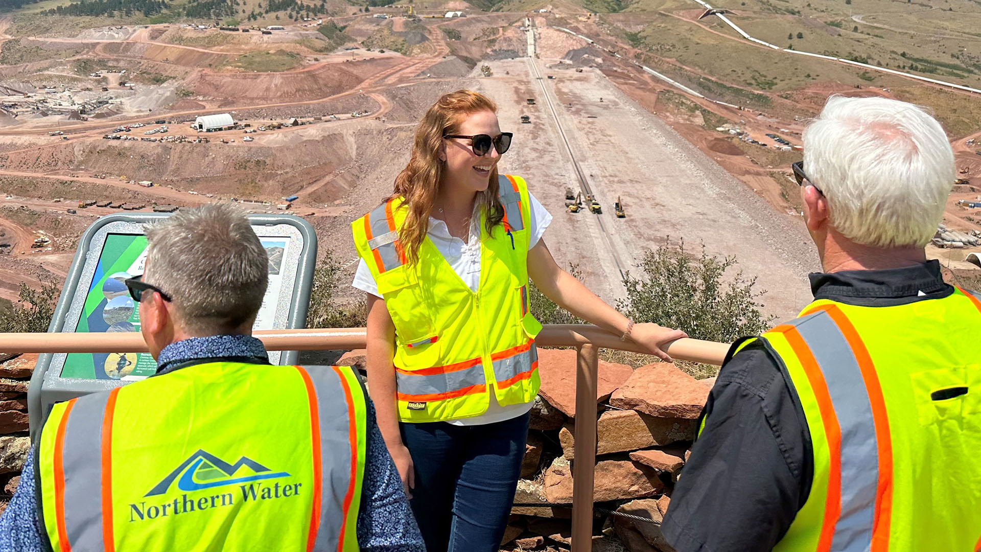 Woman leading a tour standing along a railing high above construction.