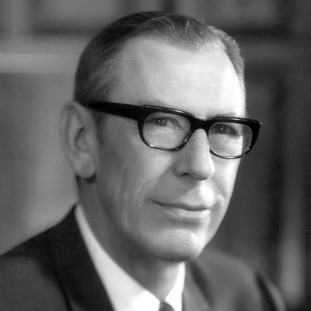 Grayscale image of a man wearing black glasses in a suit.