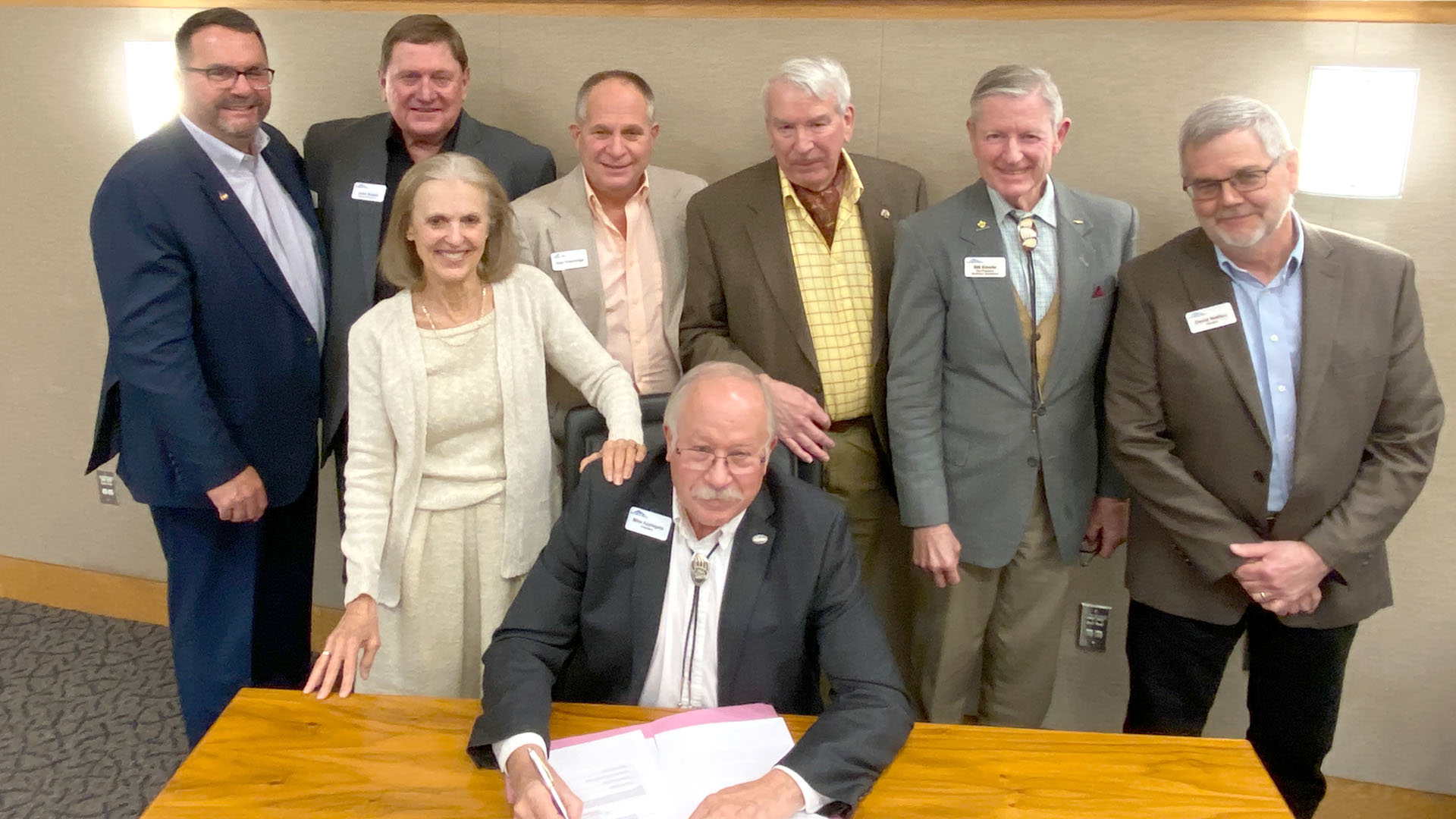 People standing around one man who is signing a document into effect.