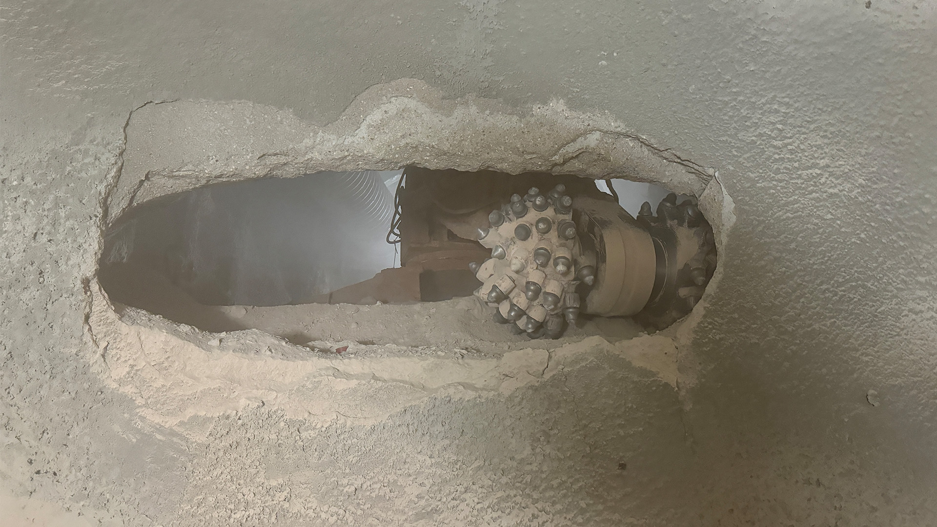 Photo of a roadheader seen through a cut in the tunnel wall connecting the downstream and upstream sections. 