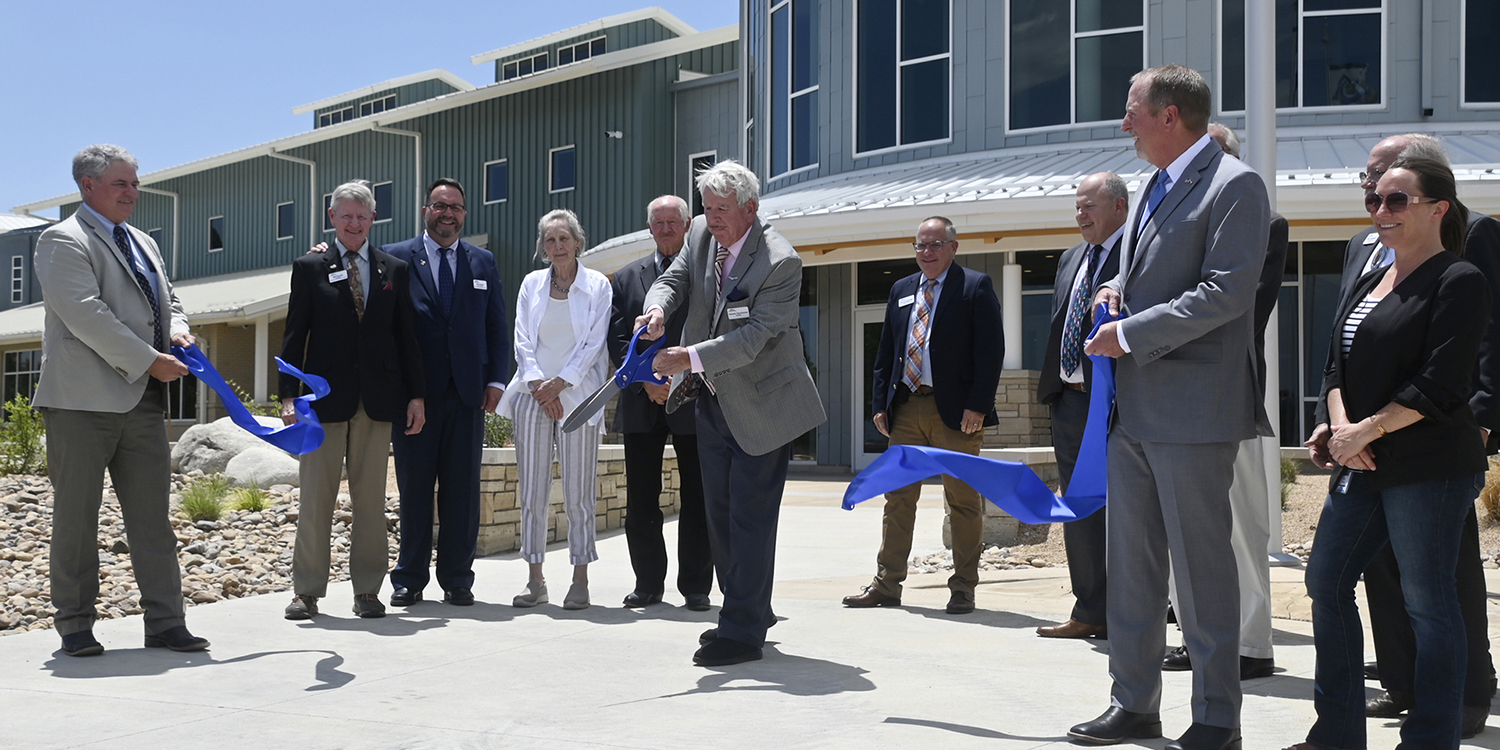 Board President Dennis Yanchunas cuts scissors at a ribbon cutting with several other Board members surrounding