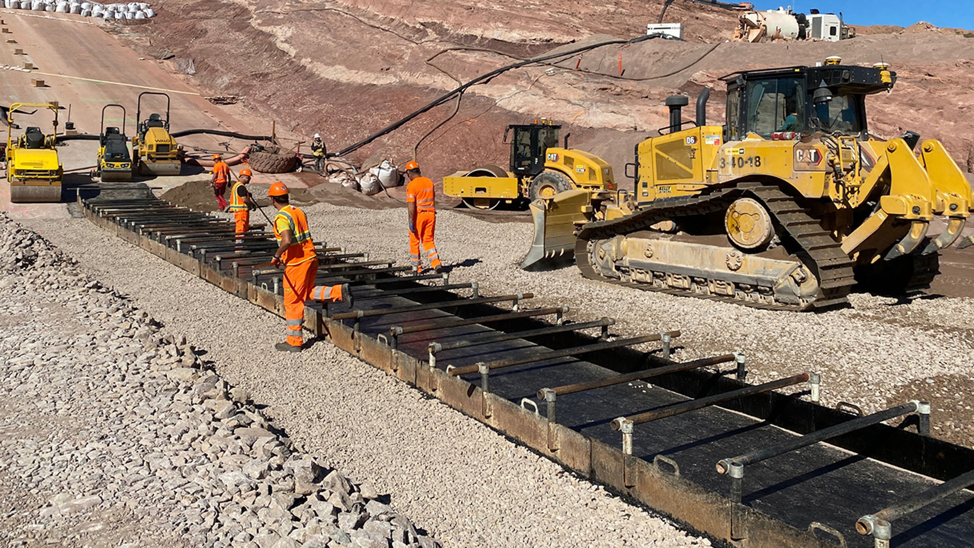 Men in orange suites laying down the forms for an asphalt placement on a dam.