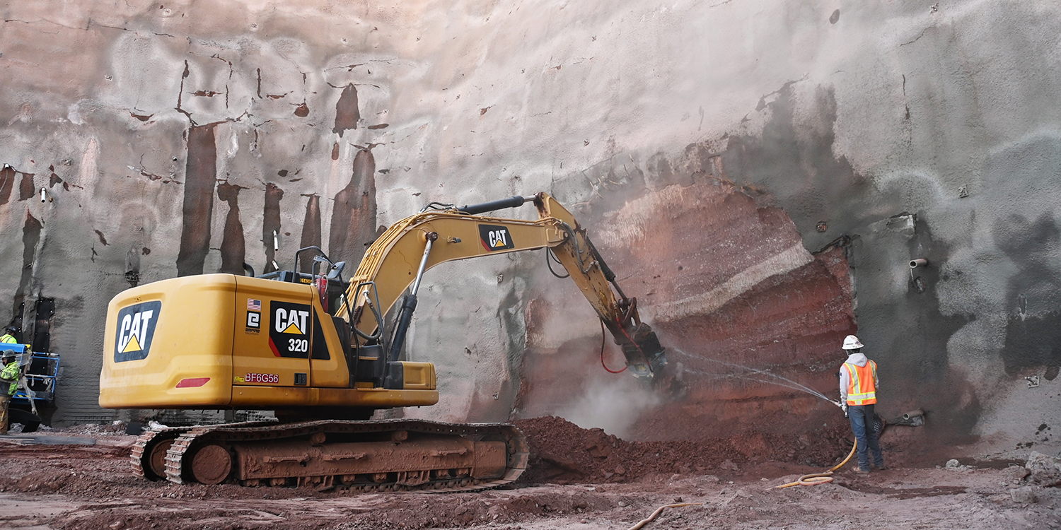 Man spraying water while machine cuts into the downstream portion of the tunnel on April 4, 2022.