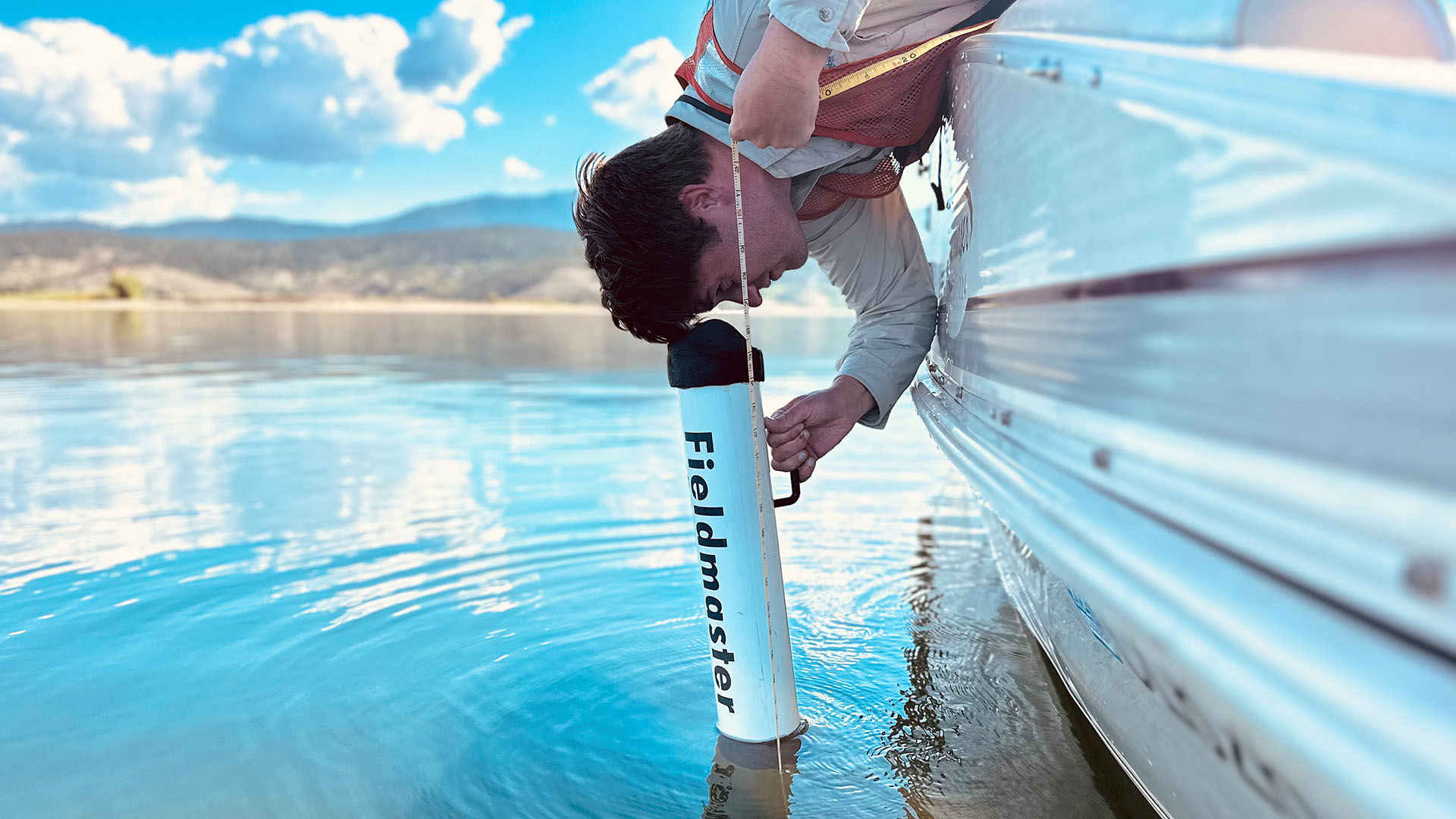 Man leaning over edge of boat to measure clarity using a viewscope.