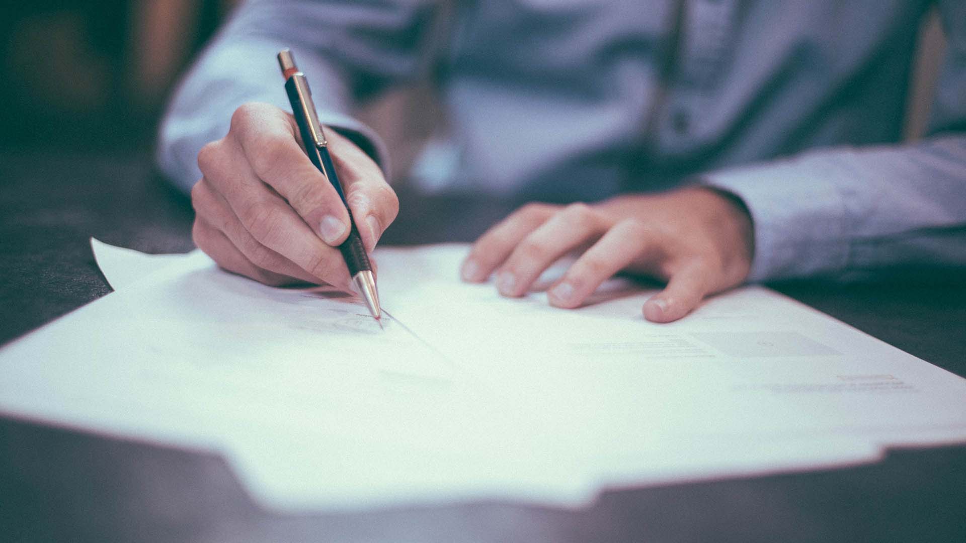 A person's hand holding a pen signing a contract.