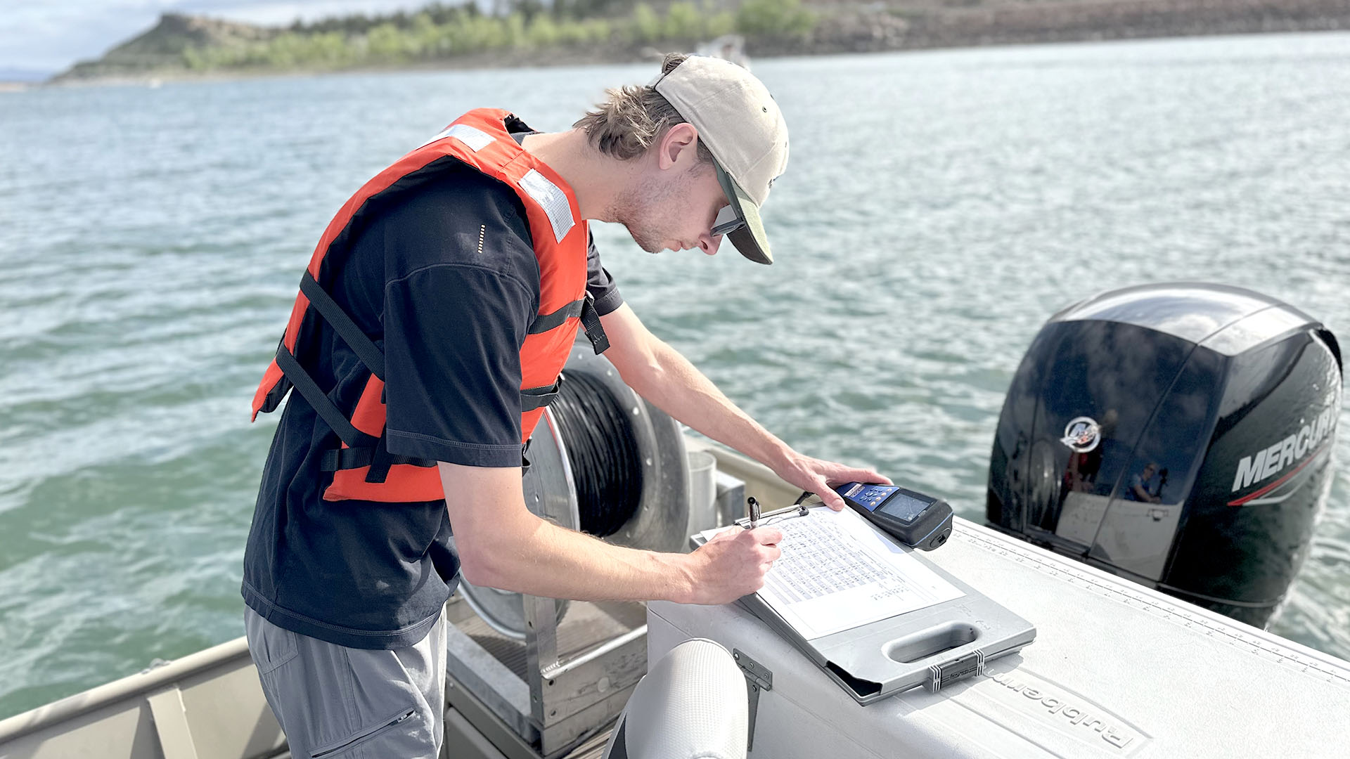 A man in a life vest on a boat tracking data on a clipboard. 