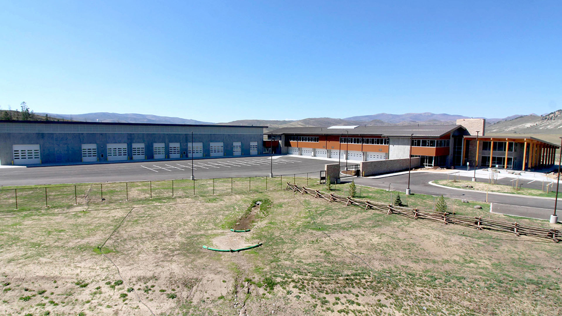 A long L-shapred building with garage doors and fence around.