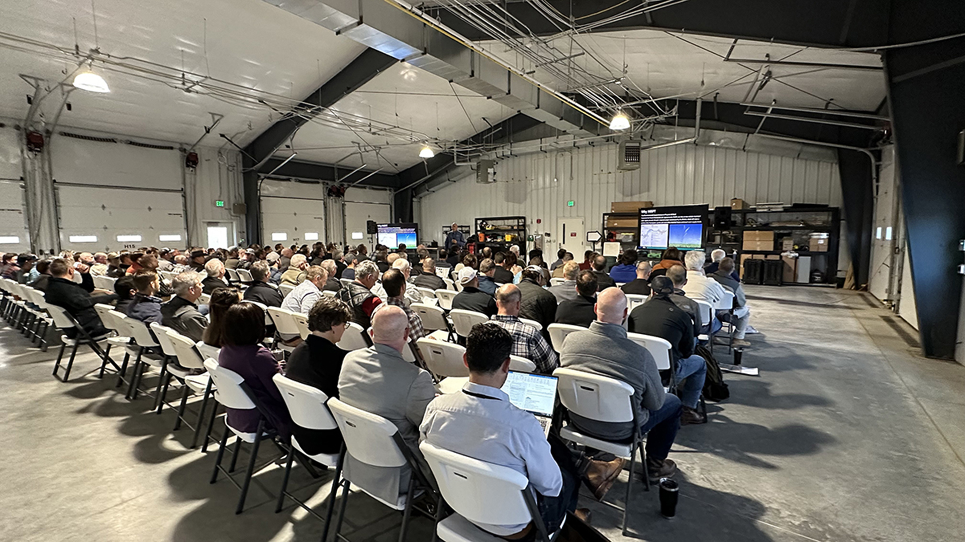 People seated in rows watching presentations in a garage.