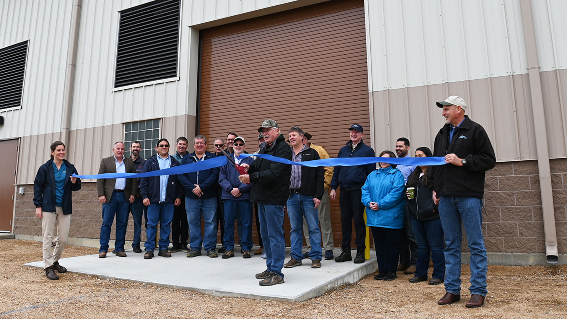 People lined up in front of a building holding a large blue ribbon to cut.