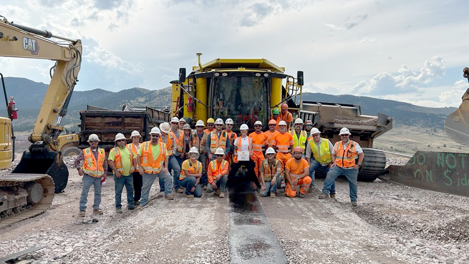 Group of people in front of a large machine celebrating the last asphalt layer.