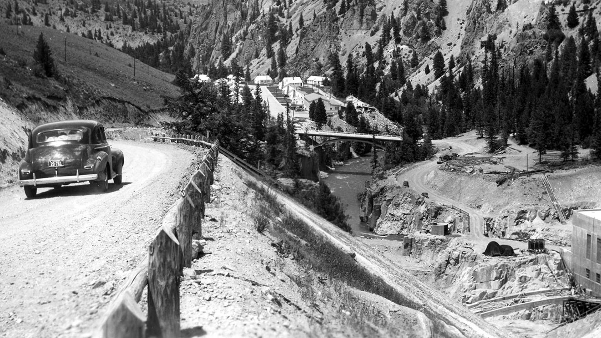 Car from 1930s along a dirt road overlooking the building of Green Mountain dam.