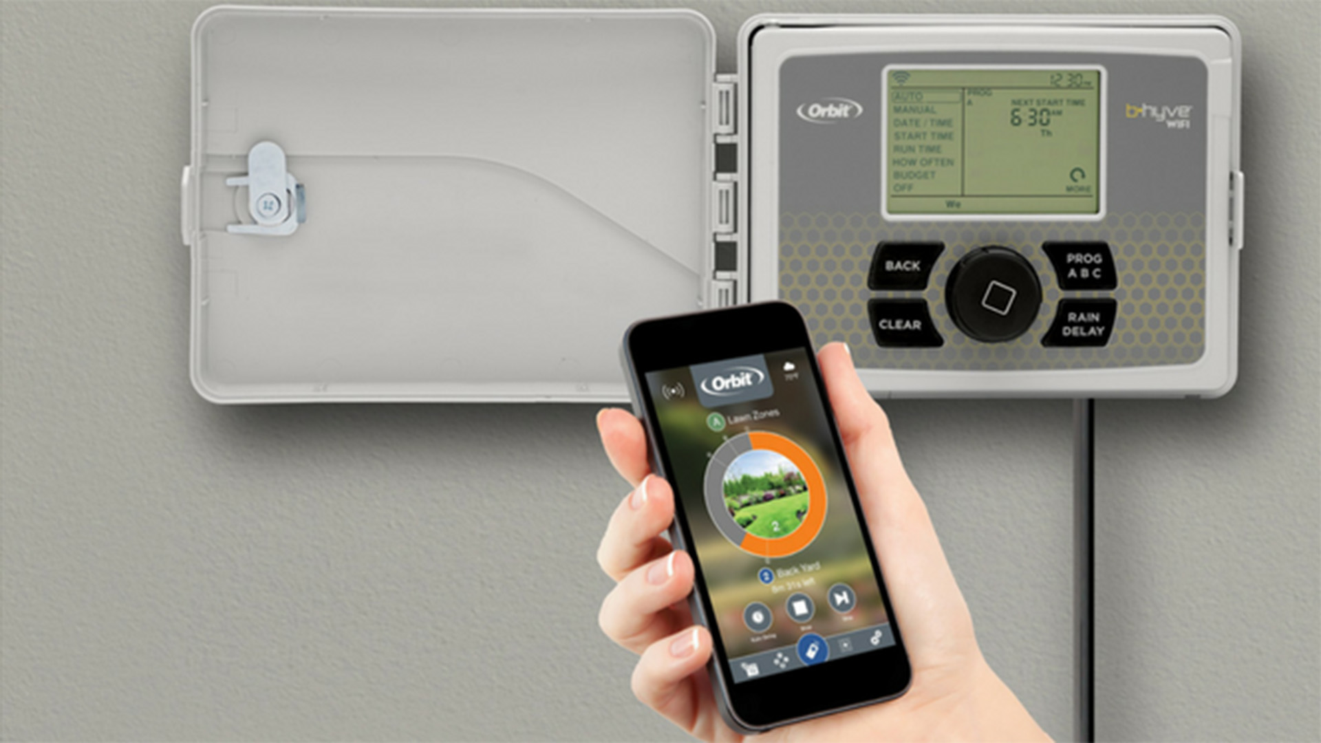 Hand holding a smart controller in front of an irrigation control panel