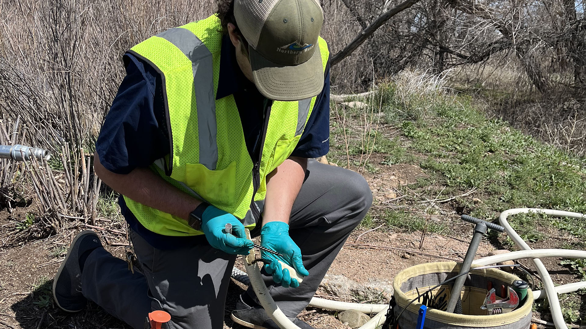 A man wearing a hat and high vis vest conducting salinity monitoring holding a tube and other tools for the job. 