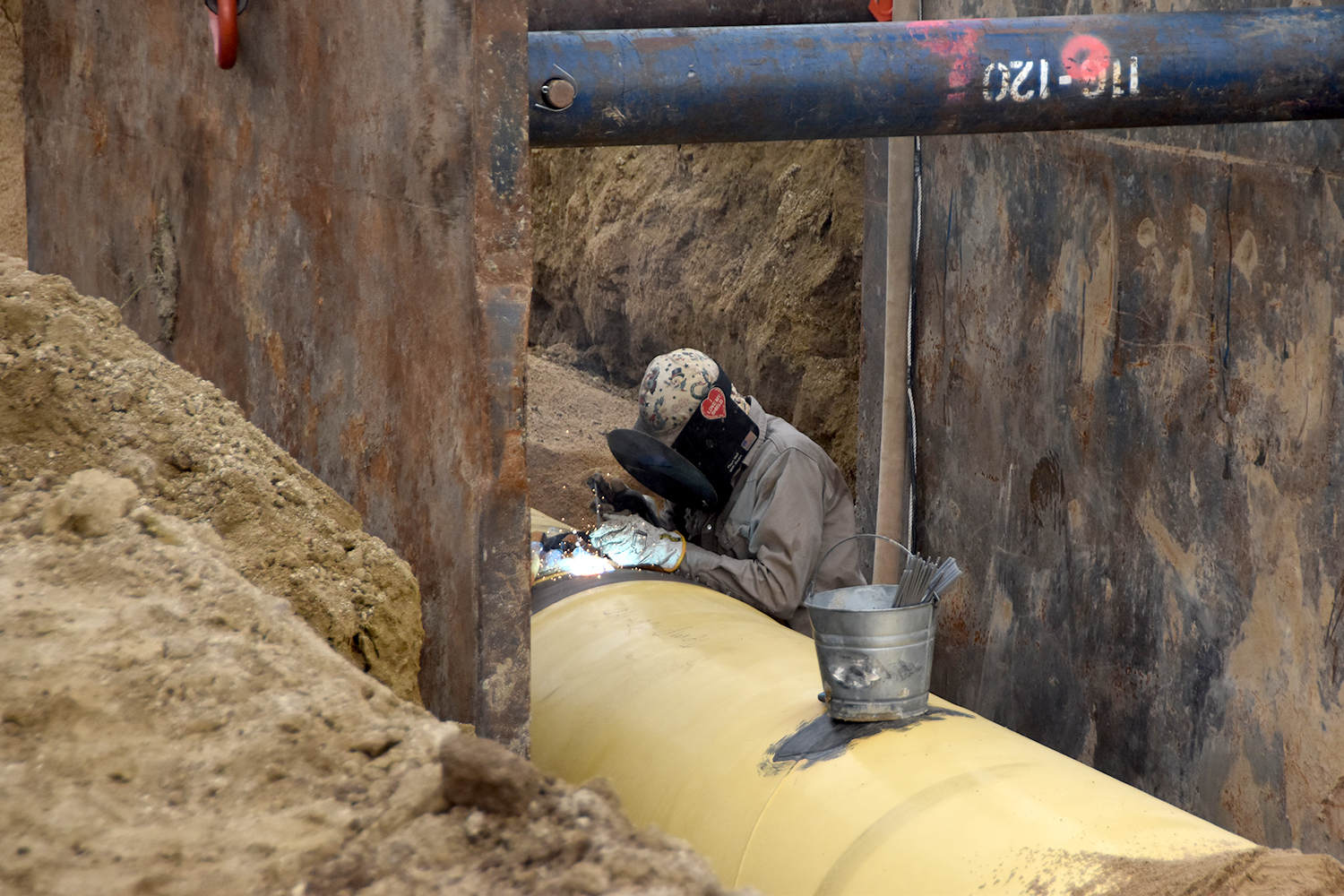 Man welding on a water pipeline in a trench with the trench box around him.