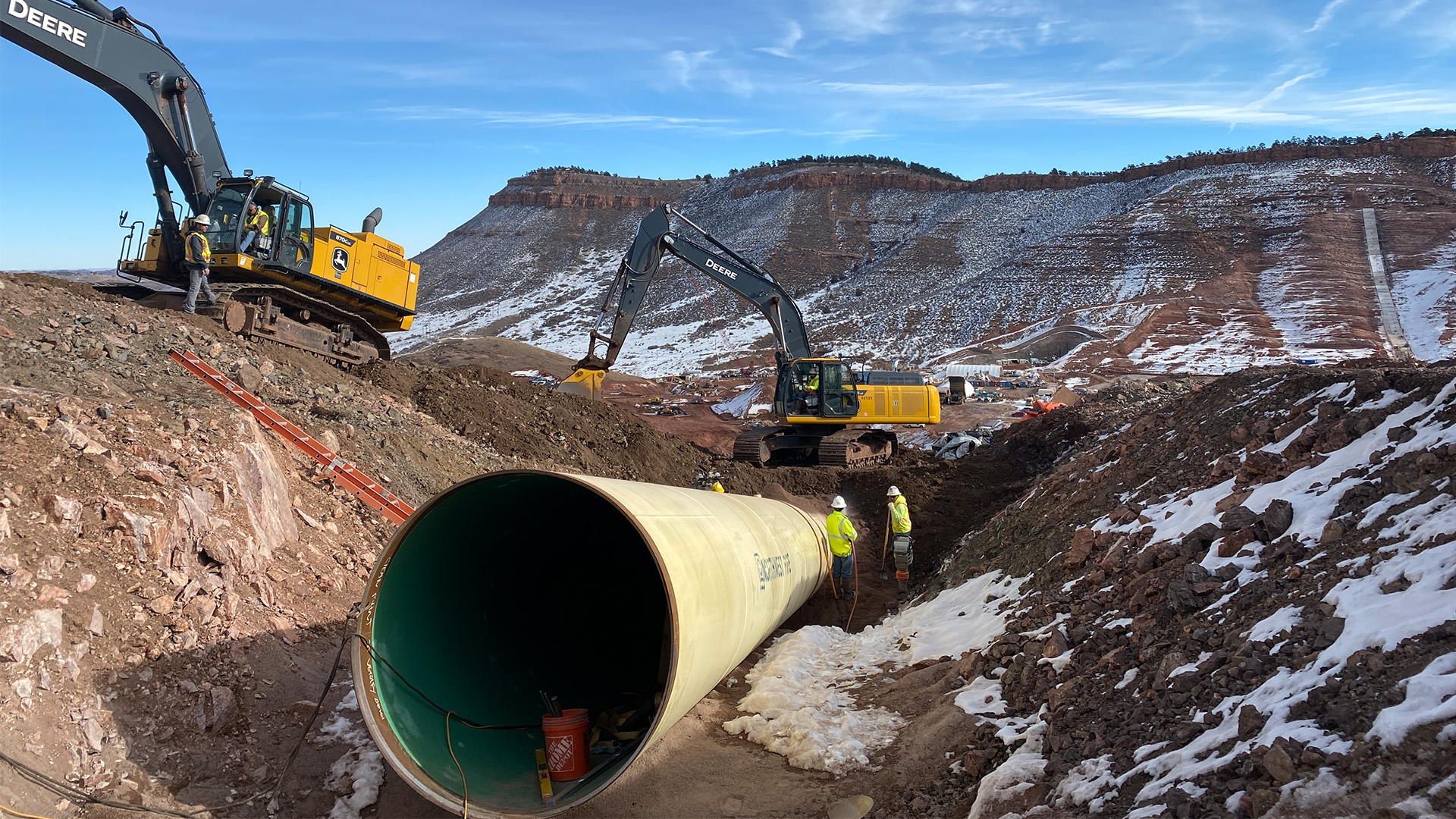 Large water pipeline being installed in the ground. Equipment and people around.
