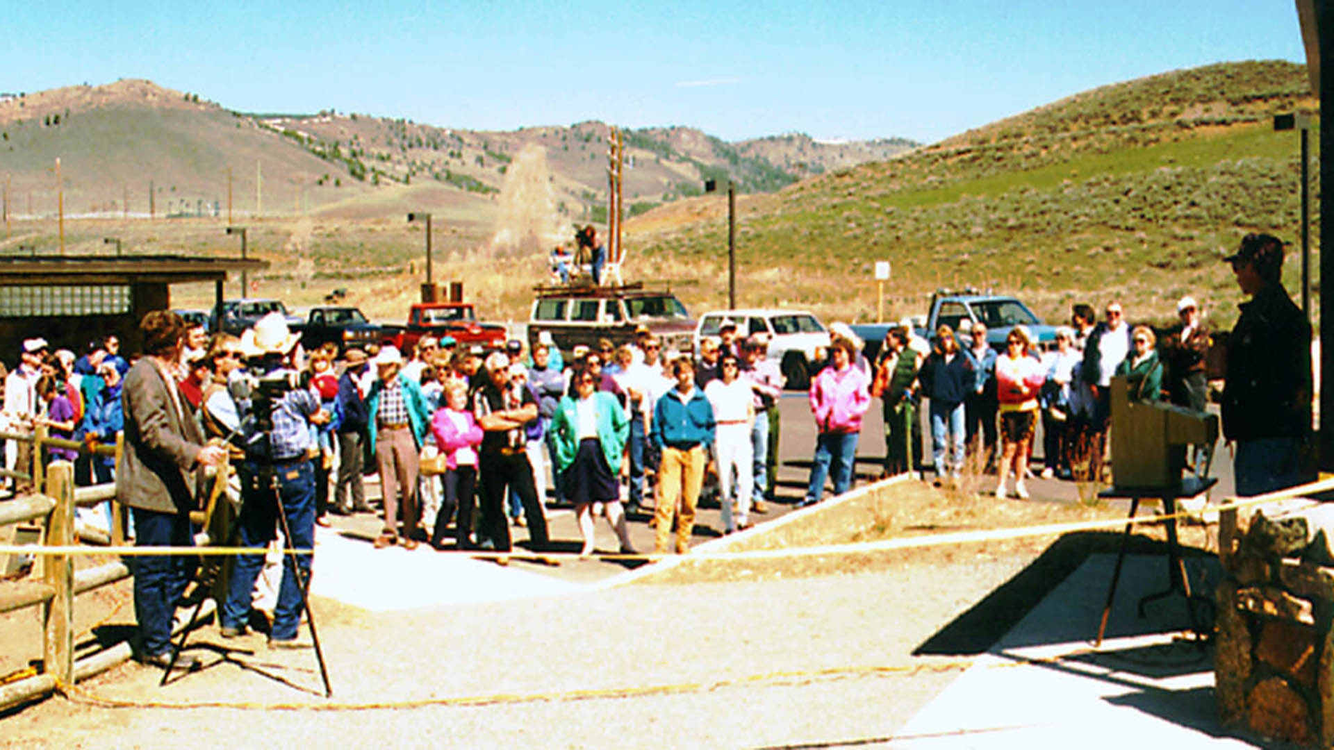People standing listening to a speaker at a podium.