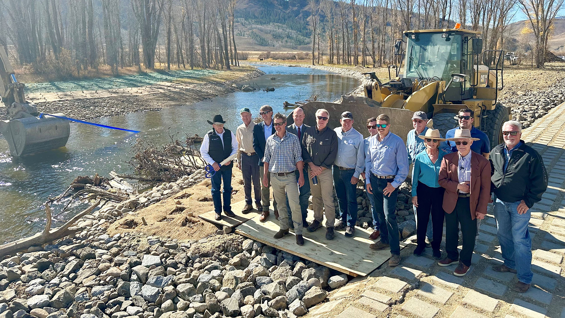 People lined up alongside a river with equipment around it celebrating a ribbon cutting.