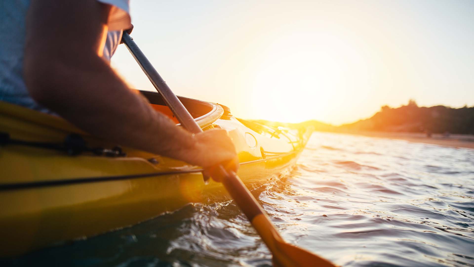 Person in kayak padding with sun setting in background.
