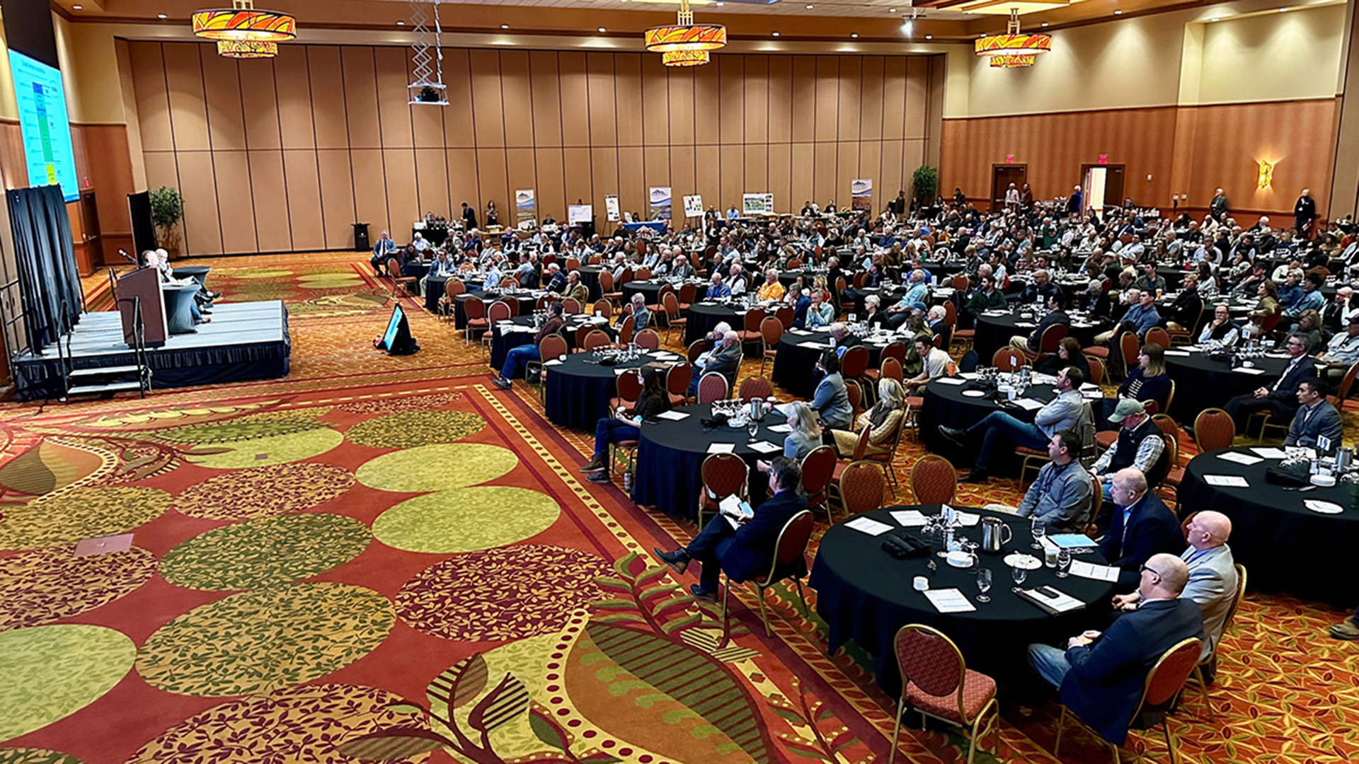 People sitting at tables in a large room listening to speakers.
