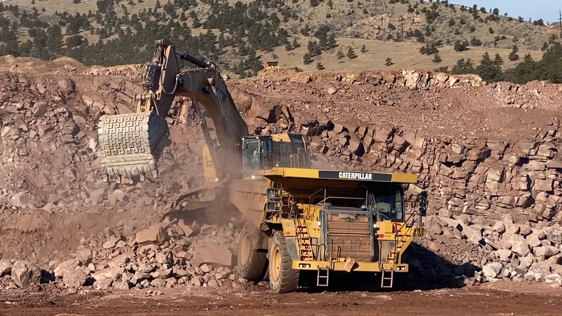 Backhoe loading Catepillar 777 truck with rock from quarry