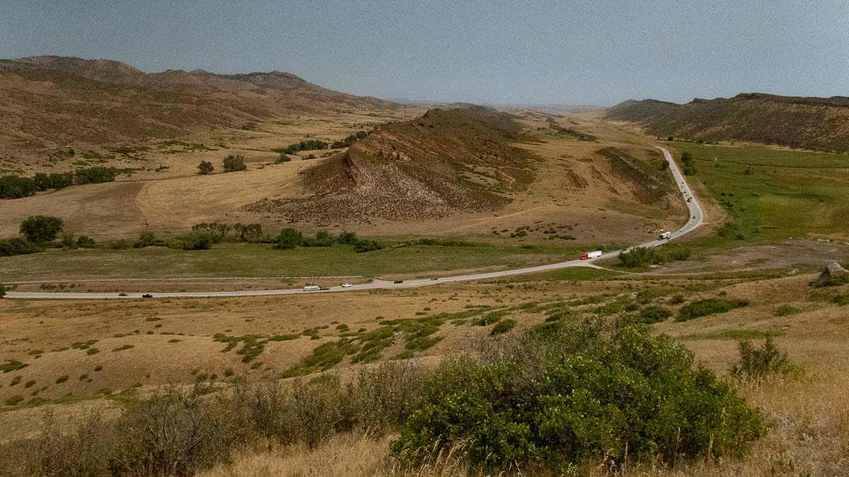 A highway runs through a valley with grass, trees and shrubs