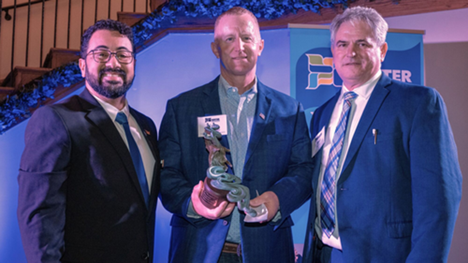 Three man posting with the center man holding an award.