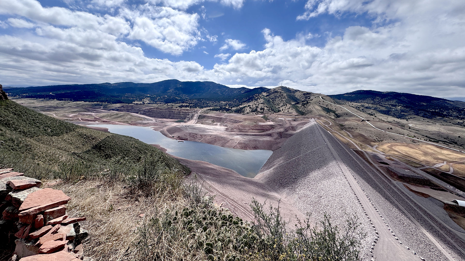 Overview photo showing a water dam with water behind it. Mountains in background.