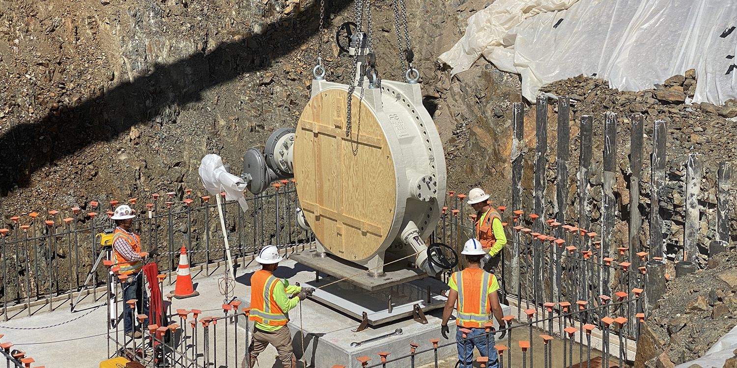 Four construction workers guide in a 72-inch butterfly valve that is being held by a crane.