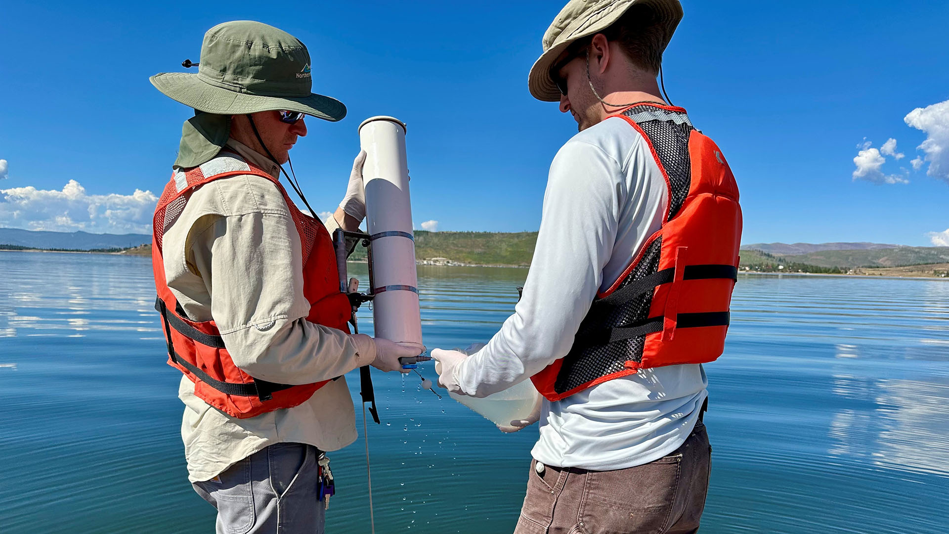 Two people doing water quality sampling from a boat in a lake.