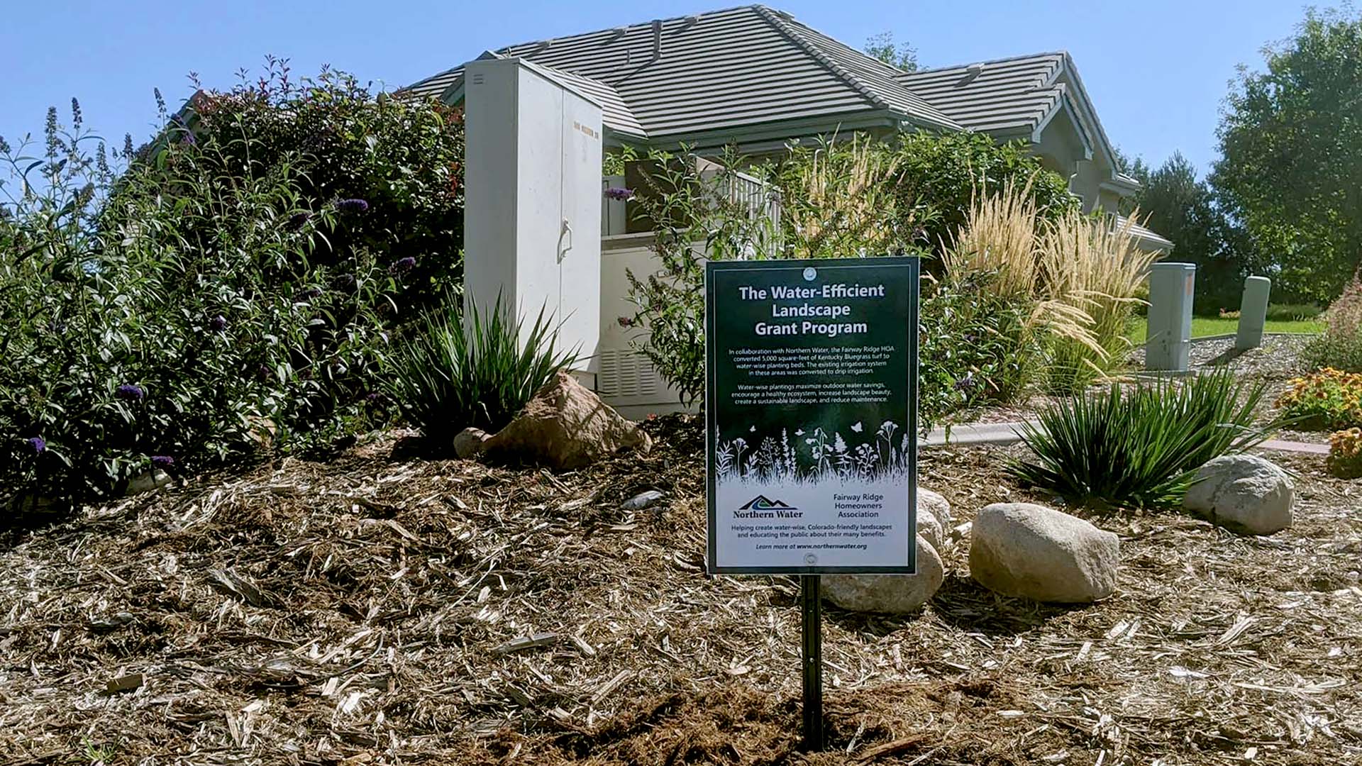 Landscape sign in the middle of a mulch bed with plants.