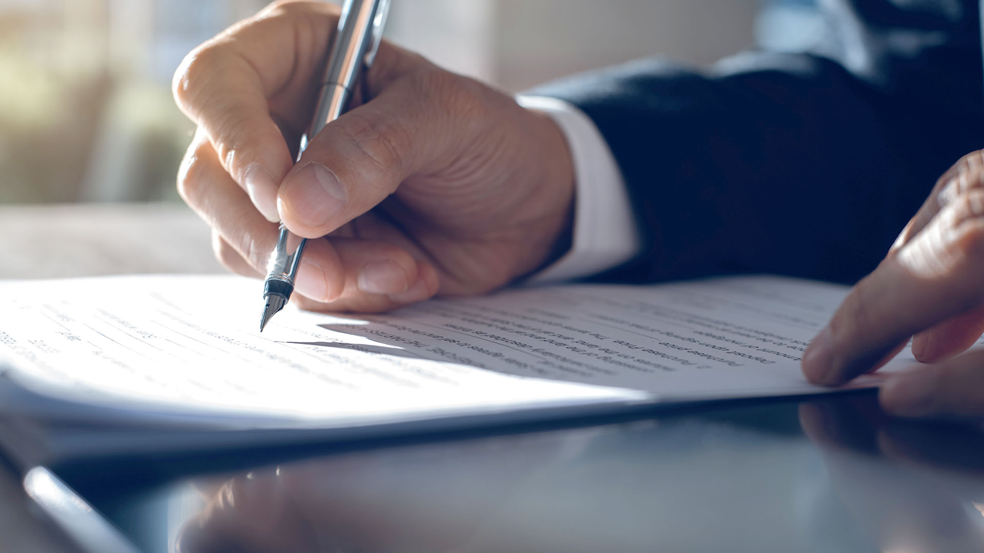 Man wearing a suit signing a contract.