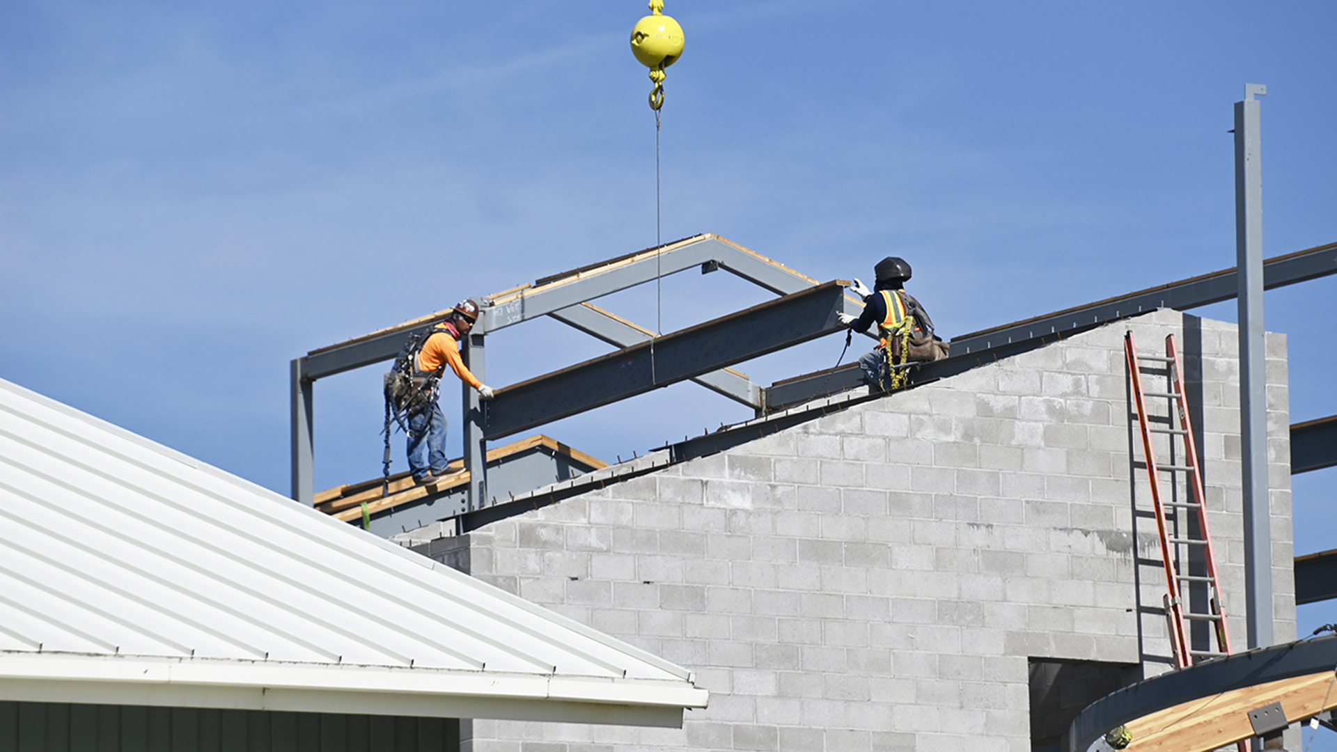 Two men wearing hardhats lifting a beam into place on top of a building.