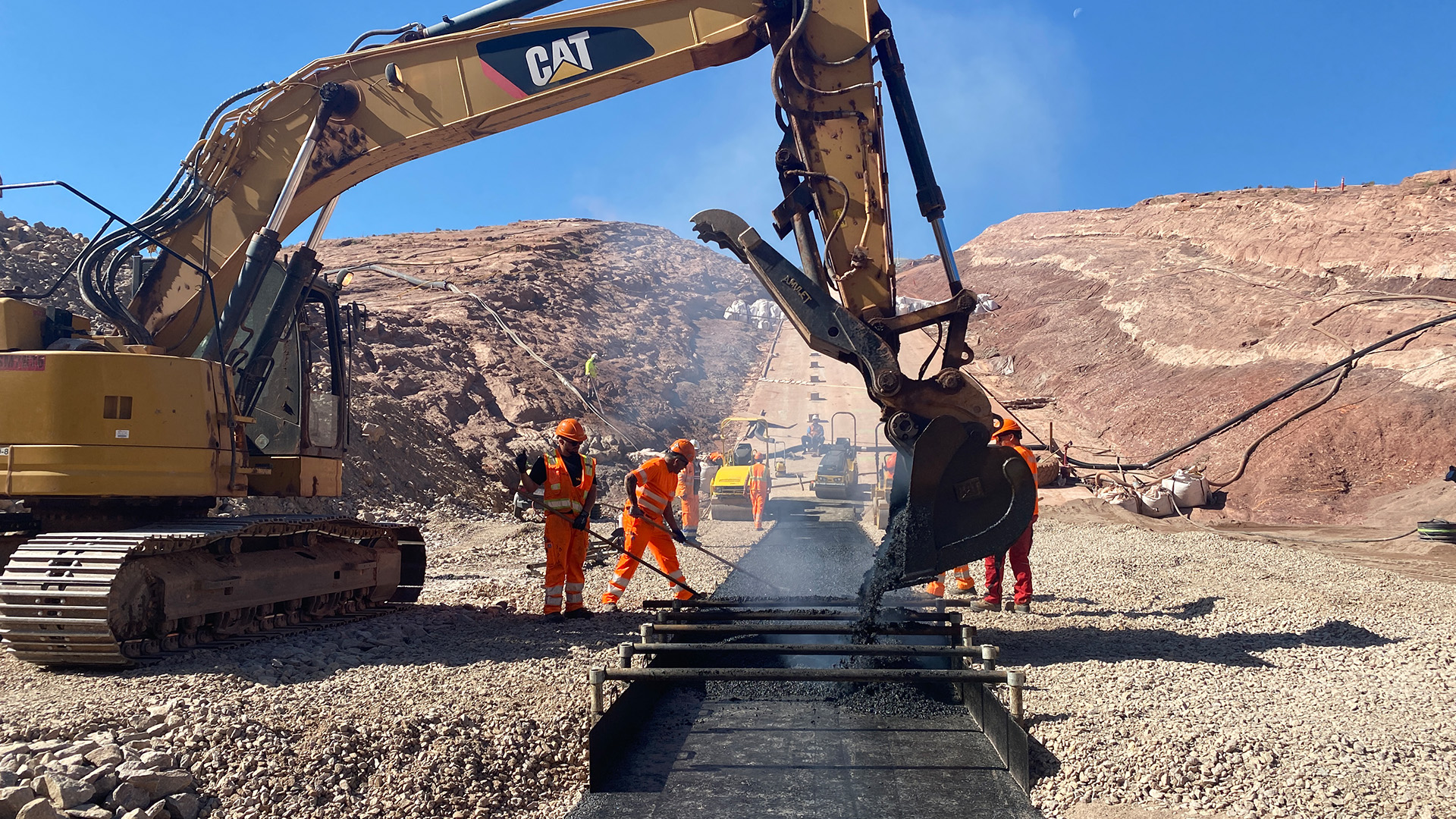 Crews placing asphalt on main dam as excavator dumps asphalt.