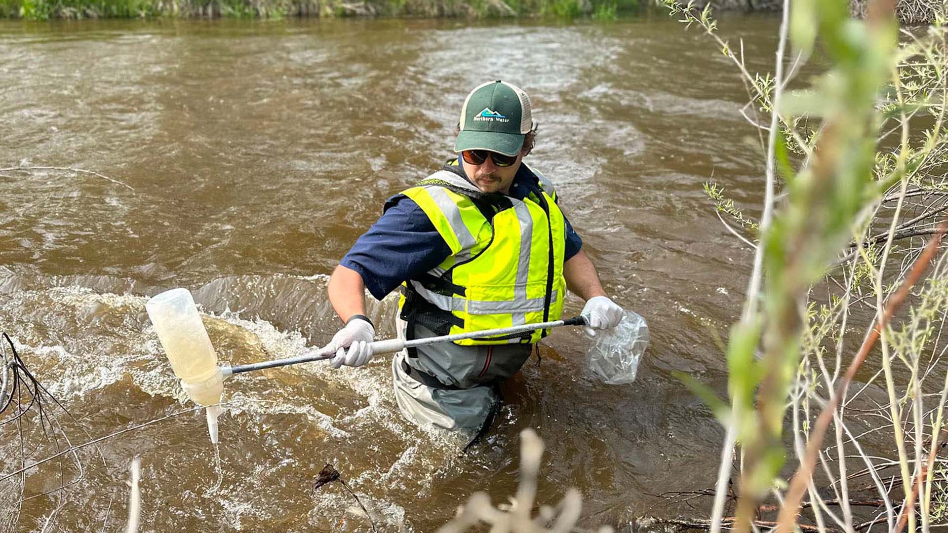 Man standing in river up to waste collecting water quality samples.