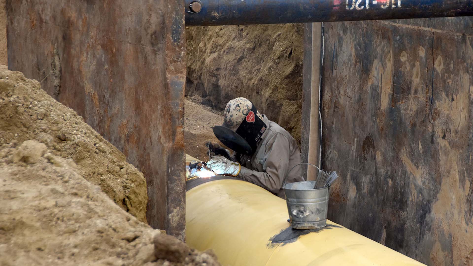 Man in a trench welding on a water pipeline.