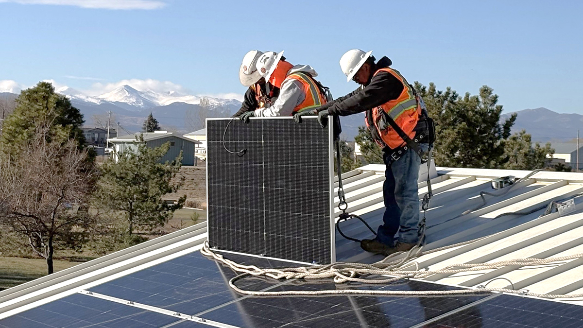 Men standing on a roof installing solar panels.