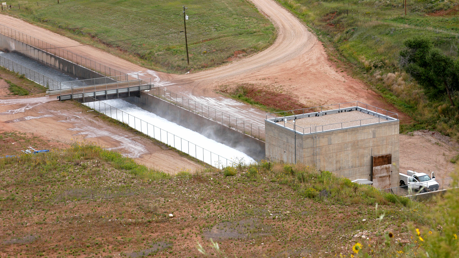 A small building with water flowing out of it under a bridge.