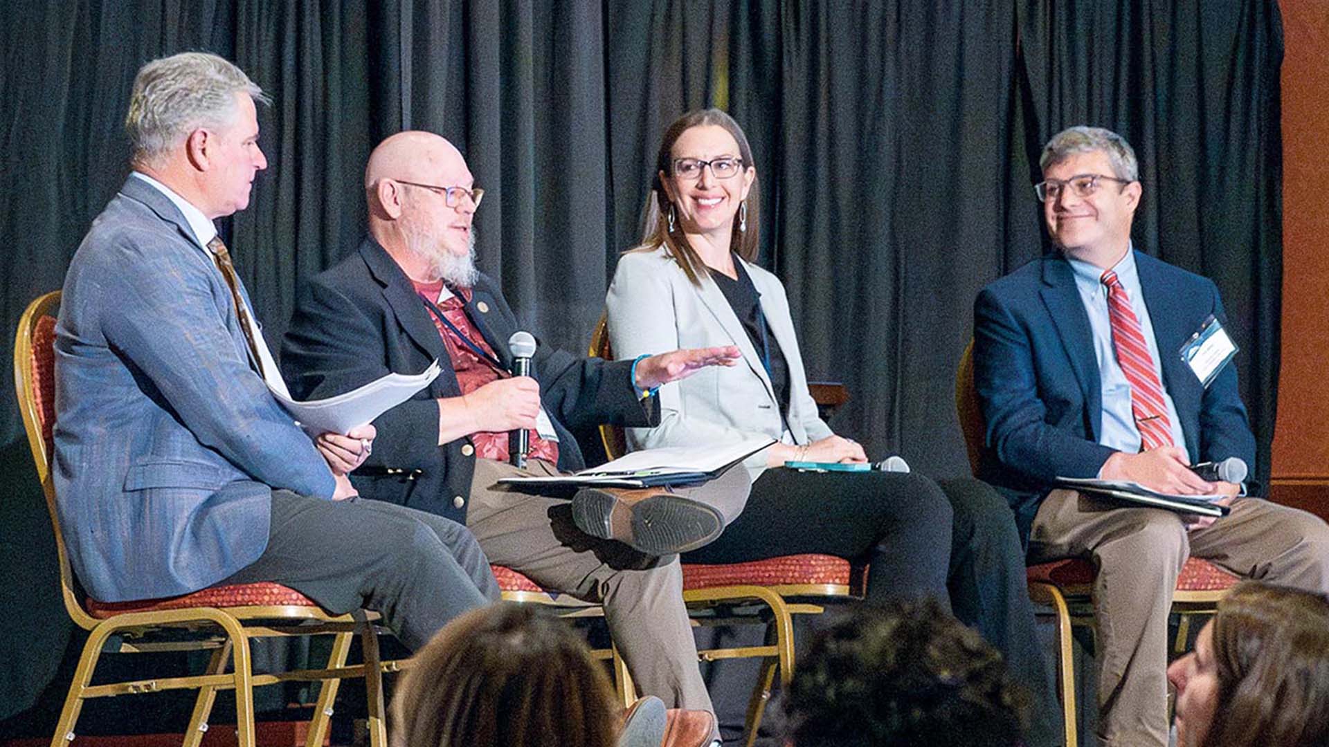 Four people on stage at a Symposium event.