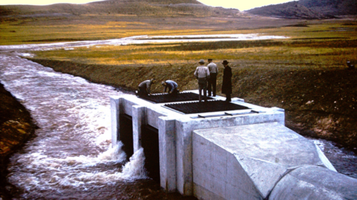 Historic photo of Carter Lake with six people standing on top of a structure while water enters the reservoir for the first time