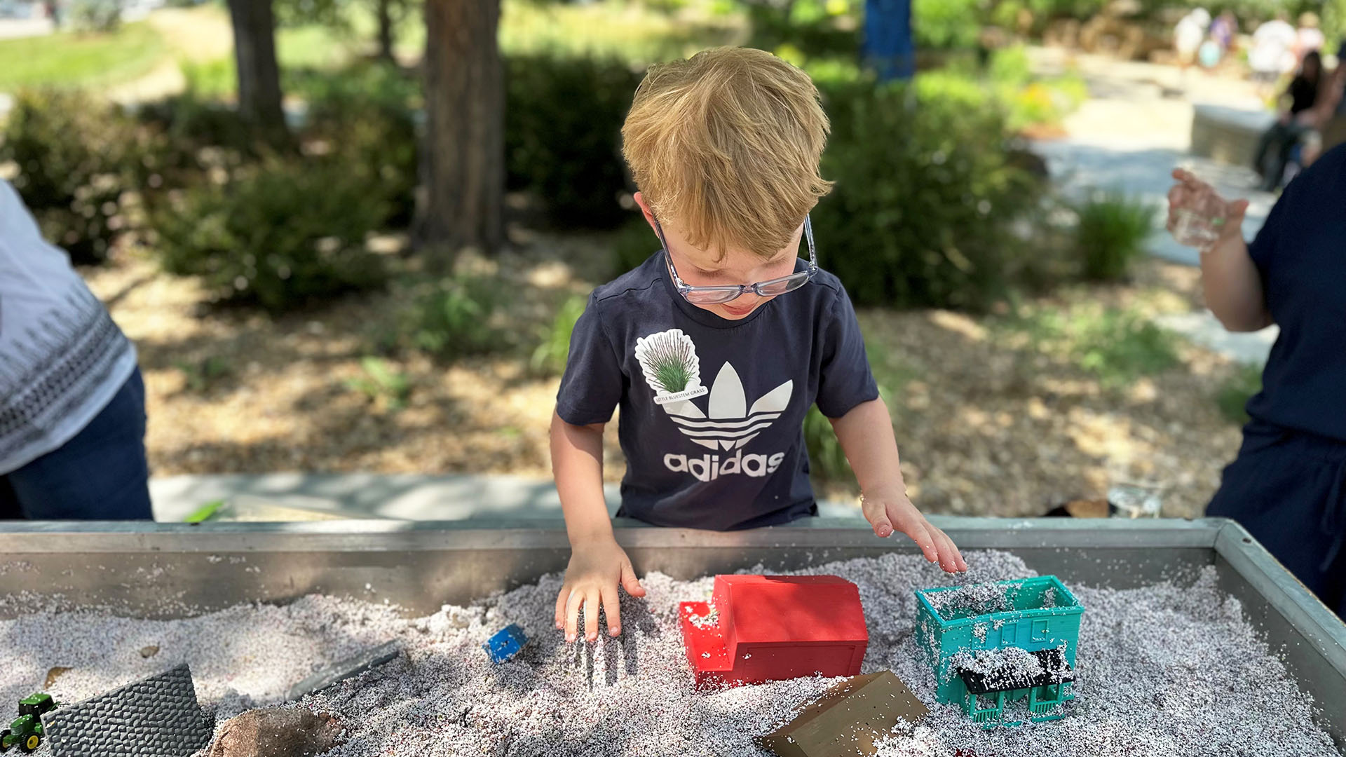 A young boy playing at a table with sand and house pieces. 