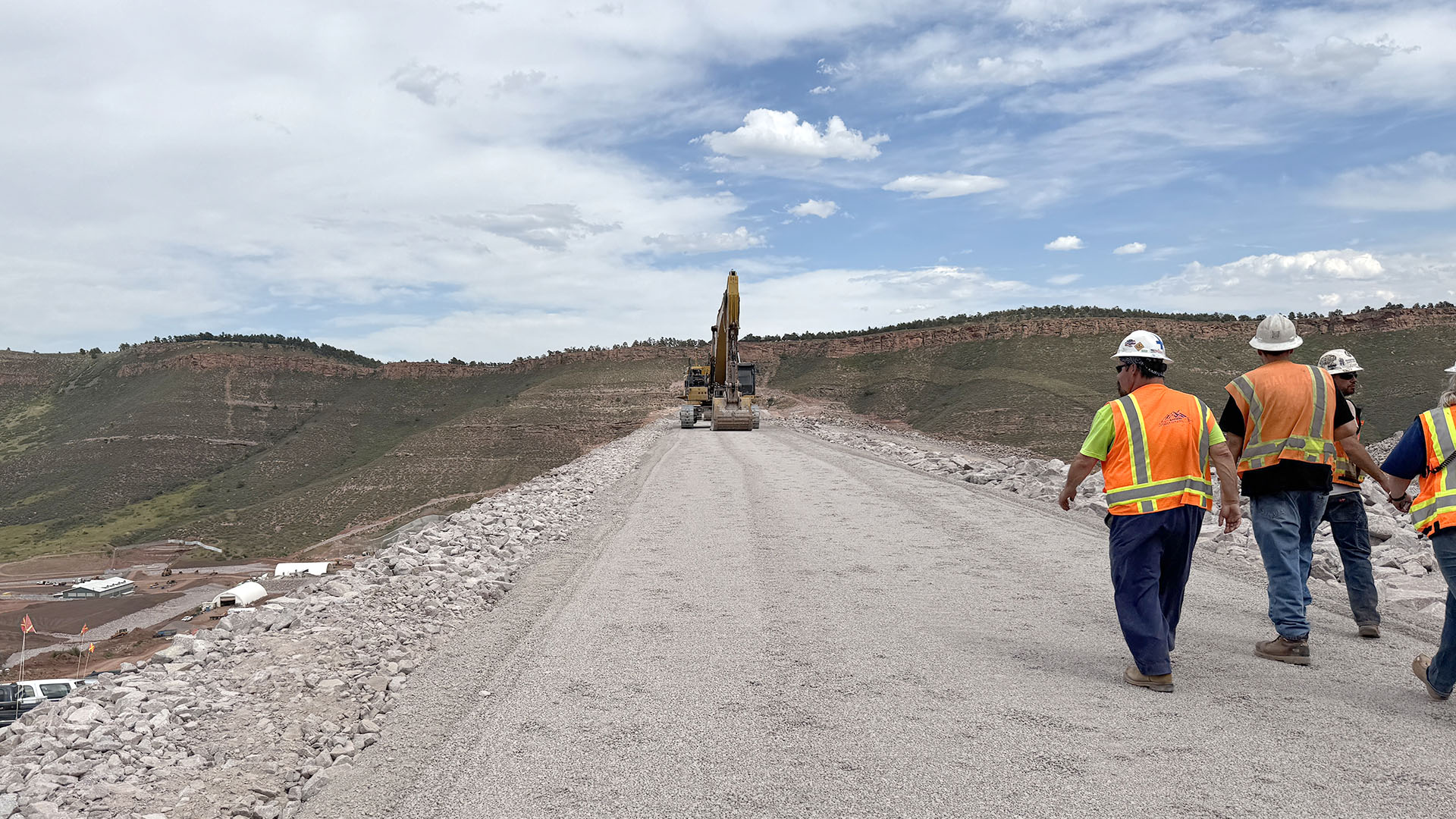 Men in orange vests walking across the finished dam. 