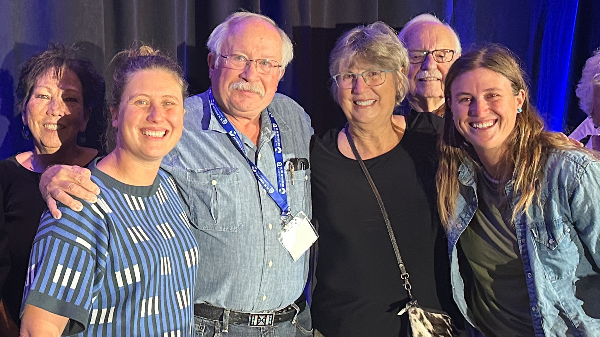 Four people pose for a picture on a stage with two people in the background